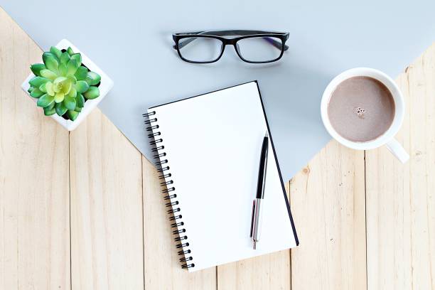 istock Top view or flat lay of open notebook with blank pages and coffee cup on office table 947206366