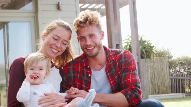 Happy white couple and young daughter sitting outside house