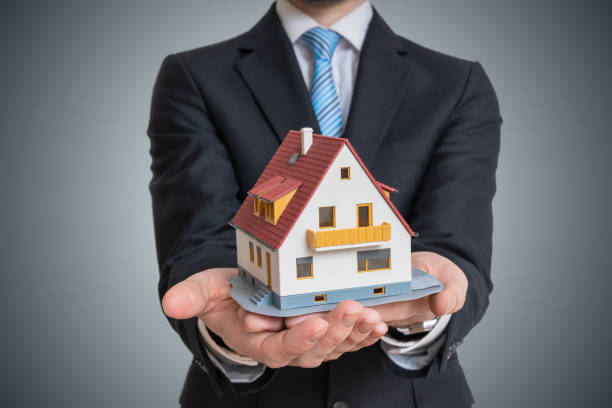 istock Real estate agent is holding small house in hand. 947219890