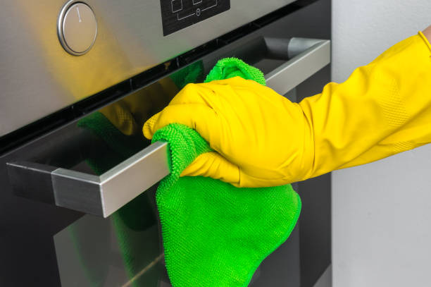 istock Hand in glove with green rag is wiping oven in kitchen 947220862