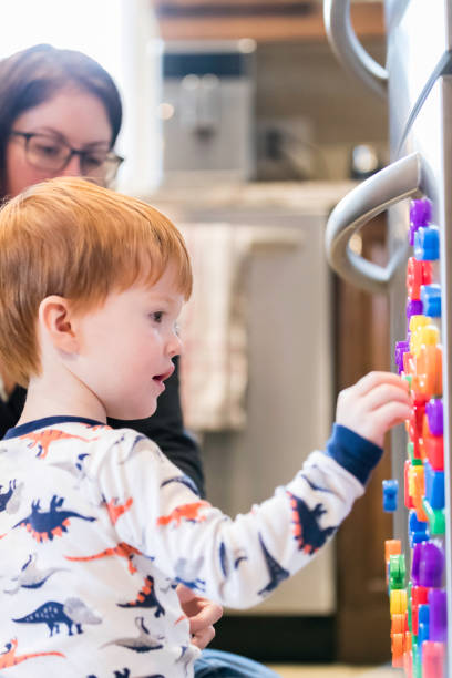 istock Cute Baby Boy Playing with Mom and Magnet Letters Text on Refrigerator 947229162