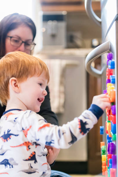 istock Cute Baby Boy Playing with Mom and Magnet Letters Text on Refrigerator 947229168