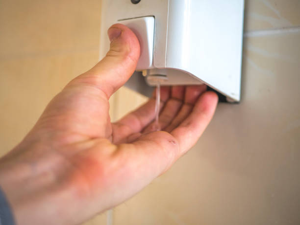 hand take liquid soap from a box on the wall to wash hands