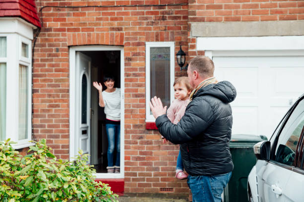 Waving Goodbye to Mum Father is carrying his baby daughter to the car and is turning round to wave at the mother who is stood at the front door of the house. northern europe family car stock pictures, royalty-free photos & images