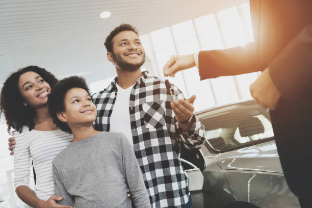 famiglia afroamericana in concessionaria auto. il venditore sta dando le chiavi per una nuova auto. - car african descent shopping car dealership foto e immagini stock