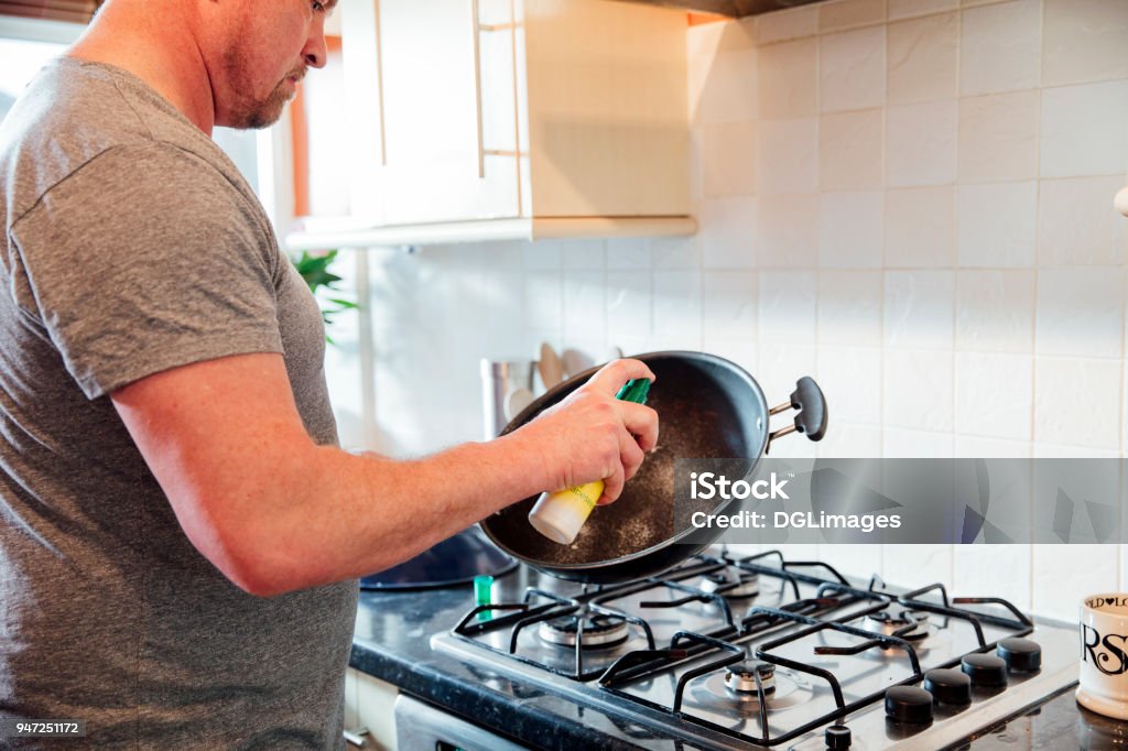 Preparing the Pan with Frying Oil Close up shot of a mature man spraying some frying oil onto a cooking wok in the kitchen of his home. Spraying Stock Photo