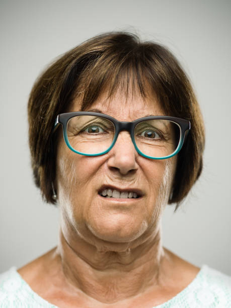 Real angry senior woman portrait Close up portrait of hispanic mature woman with displeased expression against white background. Vertical shot of real senior woman in studio. Short brown hair and modern glasses. Photography from a DSLR camera. Sharp focus on eyes. disgust stock pictures, royalty-free photos & images