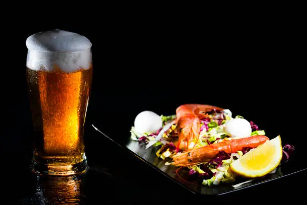 Sweated glass of cold light beer and salad with argentine red shtimp. Pfoto on dark background. Copy space