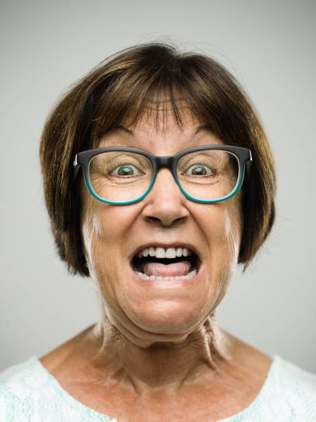 Real shouting senior woman portrait Close up portrait of hispanic mature woman with shouting expression against white background. Vertical shot of real senior woman screaming in studio. Short brown hair and modern glasses. Photography from a DSLR camera. Sharp focus on eyes. ugly face stock pictures, royalty-free photos & images