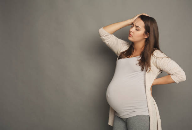 istock Young pregnant woman with headache at studio 947253012