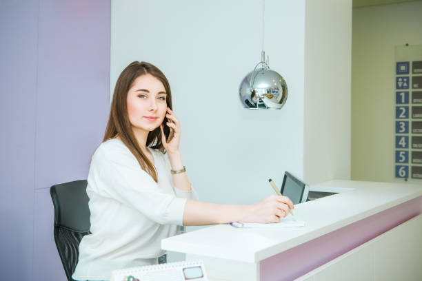 porträt der freundliche junge frau blick in die kamera, am telefon hinter der rezeption. administrator im büro, klinik, zentrum, hotel. beruf-konzept. tiefenschärfe, platz für text. - arzthelferin stock-fotos und bilder