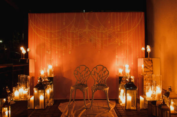 istock Two white vintage antique chairs on the candles background. Magic romantic light decoration. Candles lit and glass holders. 947264394