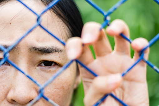 woman standing behind a fence, hand grabs steel mesh cage,close up on face