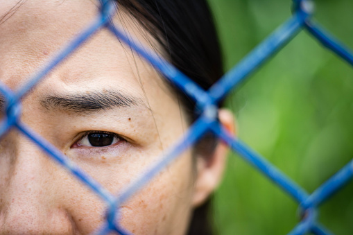 Sad woman standing behind a fence ,close up on face