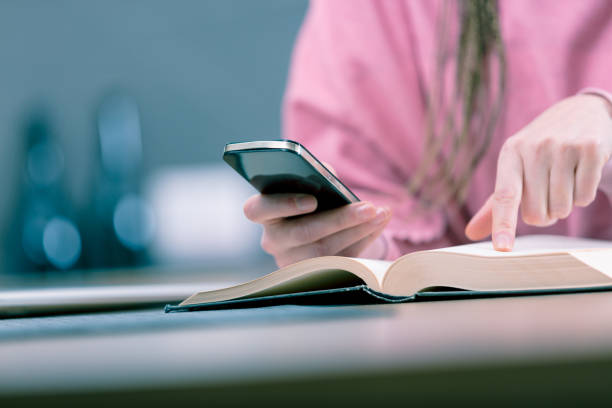 istock Woman holding mobile phone while reading book 947278690