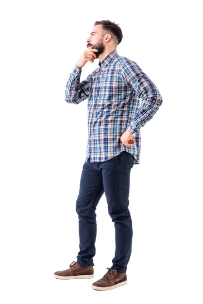 istock Young man in plaid shirt holding beard thinking and looking away. Side view. 947279480