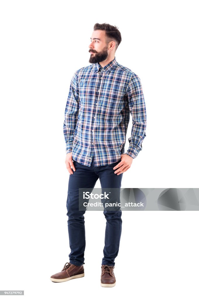 Confident relaxed bearded handsome fashion model in plaid shirt with thumbs in pockets looking away Confident relaxed bearded handsome fashion model in plaid shirt with thumbs in pockets looking away. Full body isolated on white background. Men Stock Photo