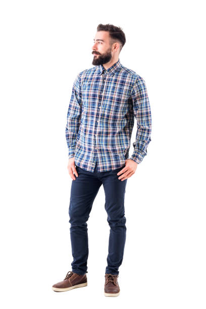 Confident relaxed bearded handsome fashion model in plaid shirt with thumbs in pockets looking away Confident relaxed bearded handsome fashion model in plaid shirt with thumbs in pockets looking away. Full body isolated on white background. man beard plaid shirt stock pictures, royalty-free photos & images