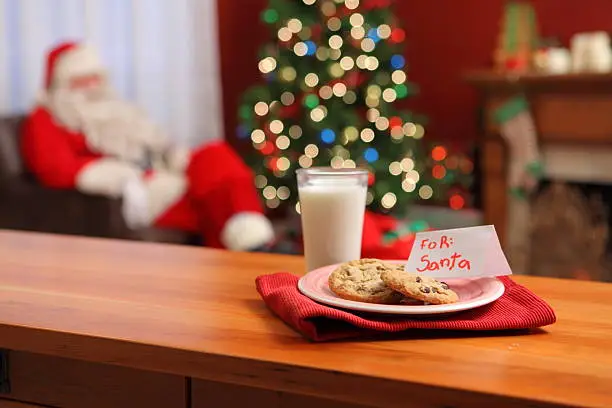 Photo of Milk and cookies on a table with a Christmas tree and Santa