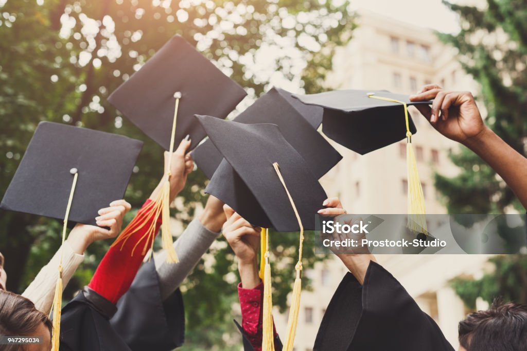 A group of graduates throwing graduation caps in the air A group of multietnic students celebrating their graduation by throwing caps in the air closeup. Education, qualification and gown concept. Graduation Stock Photo