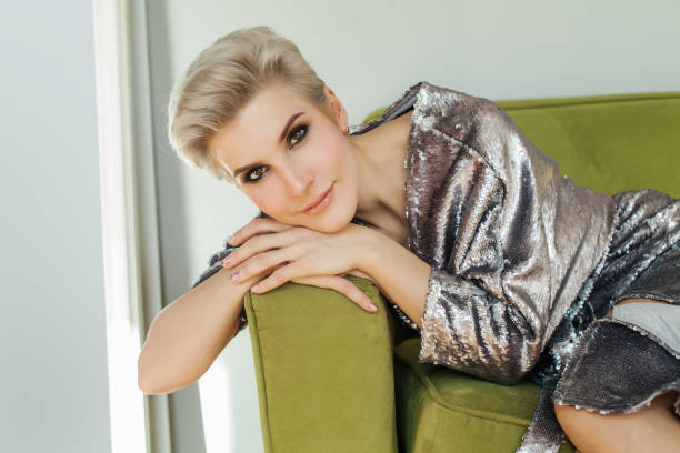 vacker blond kvinna med kort hår sitter på grön soffa. perfekta kvinnliga ansikte - mature women model bildbanksfoton och bilder