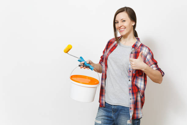 istock Young smiling woman holding empty paint bucket with copy space and paint roller and showing thumb up isolated on white background. Instruments for renovation apartment room. Repair home concept. 947302932