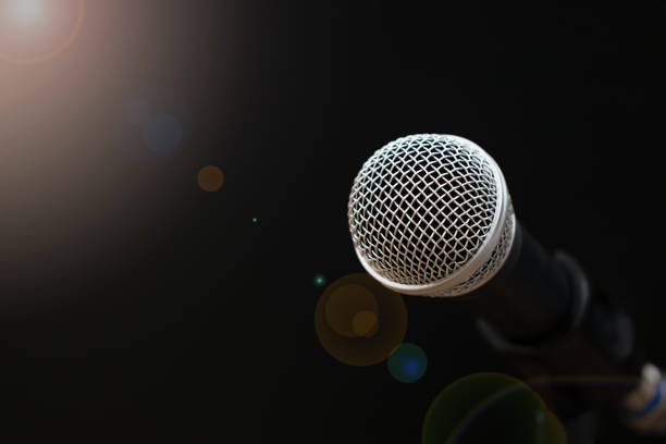istock Retro Microphones with lens light flare on front stage in pub bar or restaurant. Classic sing a song in evening and night show on black light background. 947303240