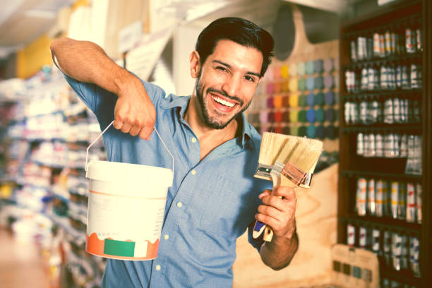 istock Man standing amongst racks in paint store with brushes and paint 947304440