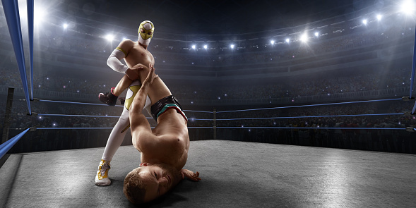 Wrestling show. Two wrestlers in a bright sport clothes and face mask fight in professional ring. Athletes perform dangerous sports stunts