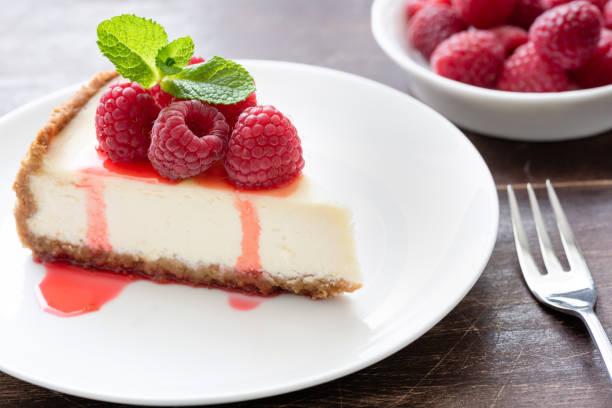 istock Slice of classical cheesecake with raspberries and berry sauce on white plate 947324128