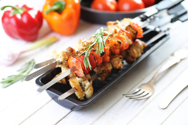 Kebab cooked on metal skewers with vegetables served on white table