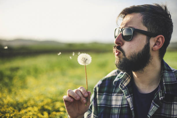 istock Young man blowing on dandelion flower 947344280