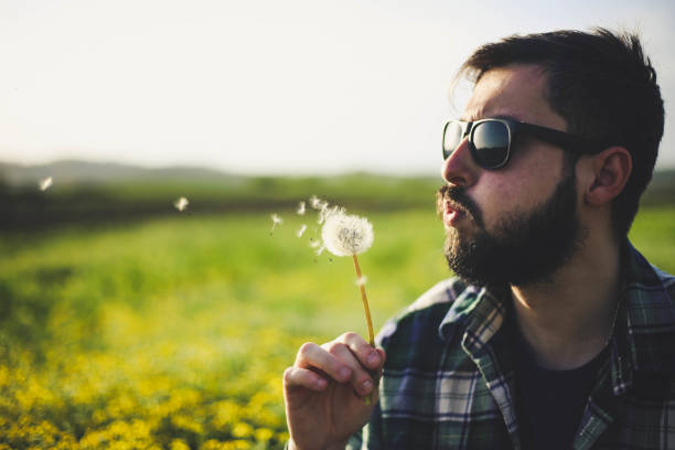 istock Young man blowing on dandelion flower 947344334