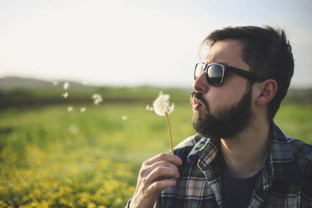 istock Young man blowing on dandelion flower 947344352