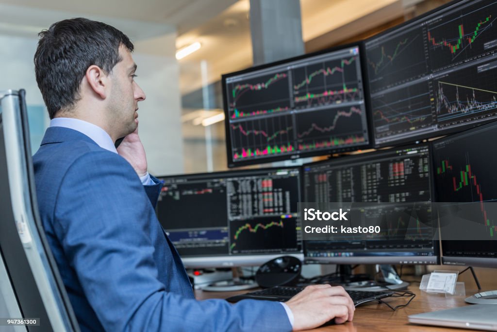 Stock broker trading online watching charts and data analyses on multiple computer screens. Male stock broker trading online watching charts and data analyses on multiple computer screens. Stock Market and Exchange Stock Photo