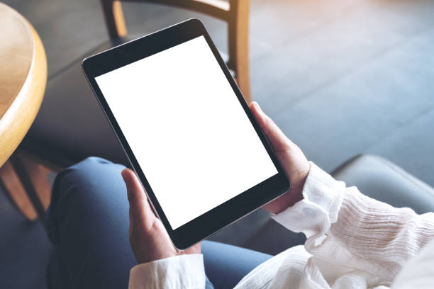 imagen de maqueta vista superior de una mujer sentada de piernas cruzadas y sosteniendo negro tablet pc con pantalla en blanco del escritorio blanco - tableta digital fotografías e imágenes de stock