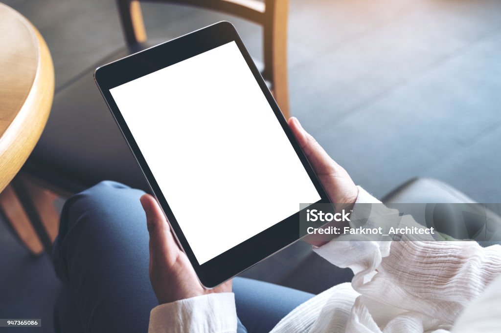 Top view mockup image of a woman sitting cross legged and holding black tablet pc with blank white desktop screen Digital Tablet Stock Photo