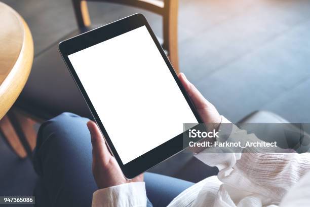 Top View Mockup Image Of A Woman Sitting Cross Legged And Holding Black Tablet Pc With Blank White Desktop Screen Stock Photo - Download Image Now