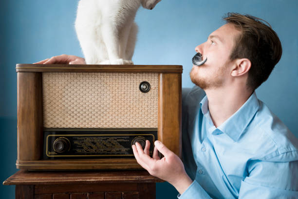 istock Mustached man playing with cat on antique radio 947382500