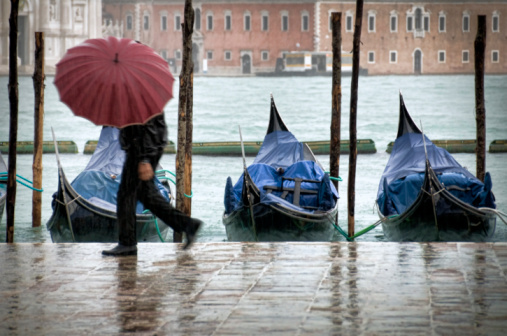 Unidentifiable pedestrian with umbrella walking along St.Mark waterfront in Venice(Italy) during a rainy winter day.