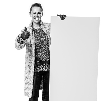 Winter things. Full length portrait of happy stylish fashion-monger in winter coat isolated on white showing blank board and  thumbs up