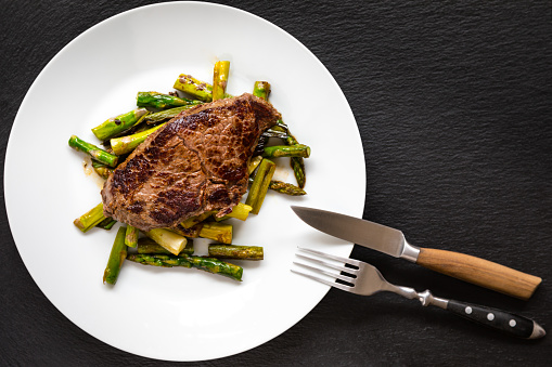 Organice beef steak with asparagus and scallion cooked with olive oil on a white plate.