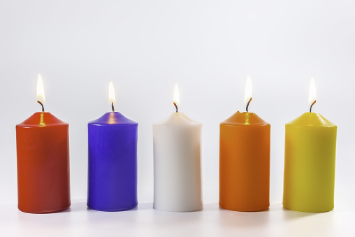 Five colors of different burning candles on a white background