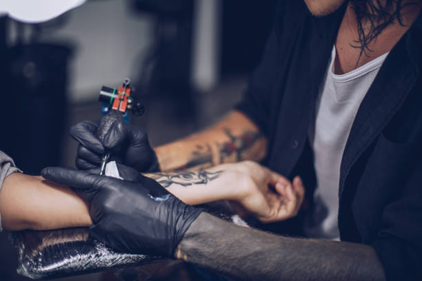 Getting arm tattoo Man and woman in tattoo studio, man is tattooing a woman's arm, part of. tribals tattoos stock pictures, royalty-free photos & images