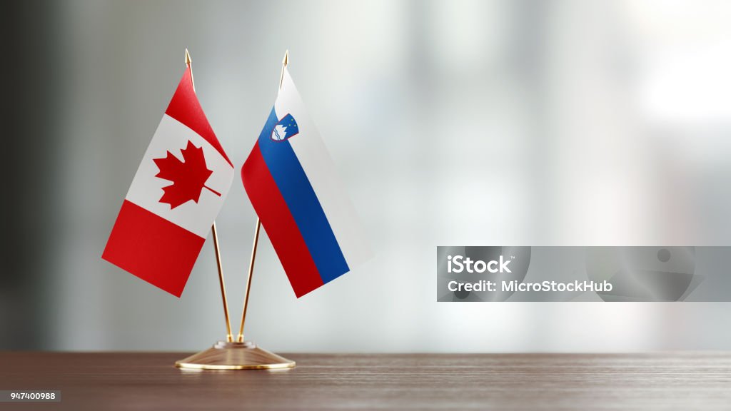 Canadian And Slovenian Flag Pair On A Desk Over Defocused Background