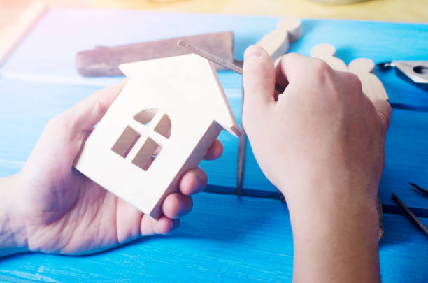 istock Men's hands make a hand-made article of wood on the background of a blue table with tools. Work at home and in the workshop. Wooden house in the hands. Concept of carpentry, home, useful occupation. 947403022