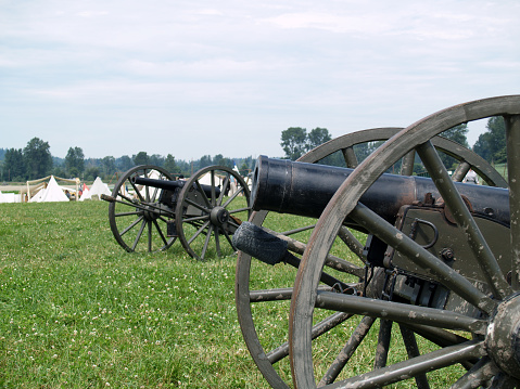US Civil War cannons in a grassy field; camp in the background