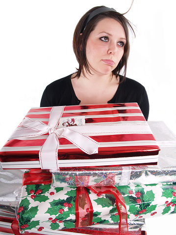 Young woman holds stack of christmas gifts and blowing upward with a tired expression