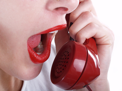 Macro of woman's mouth expressing gasp of surprise while talking on red telephone; copy space 