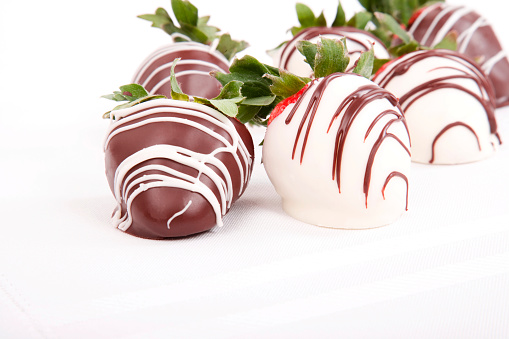 Close up of a chocolate covered strawberries; white and milk chocolate on a stark white table cloth; copy space 